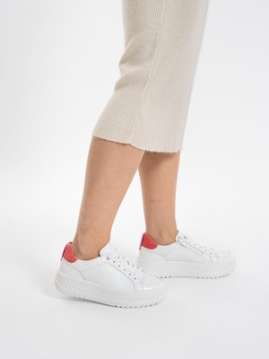 Legs wearing a beige knit skirt and white platform sneakers with pink accents, standing on a white background.