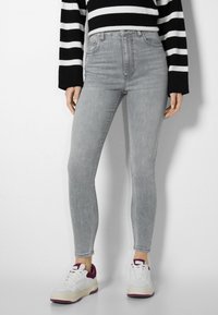 Jeans gris ajustados de cintura alta, con cinco bolsillos y un acabado desgastado, combinados con zapatillas blancas con acentos morados y una suela texturizada.
