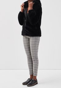 Sort faux fur zip-jakke med hætte, parret med grå ternede slim-fit bukser og sorte lakerede sko.