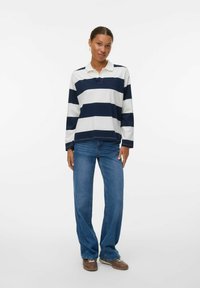 Polo a maniche lunghe a righe in blu navy e bianco, abbinato a jeans blu, con colletto e vestibilità rilassata. Calzature casual completano il look.