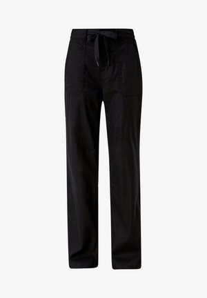 Un débardeur blanc sans manches associé à un pantalon noir ample avec poches, une taille à cordon et des sandales plates blanches.