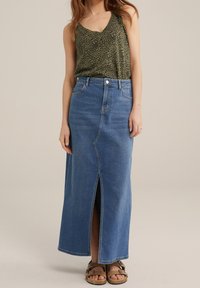 Jupe maxi en denim bleu clair avec une fente sur le devant, taille haute et design classique à cinq poches, associée à un débardeur à imprimé animal vert.