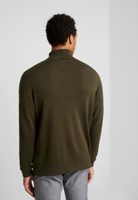 Olijfgroen gebreid trui met een hoge kraag en geribde manchetten, met een gladde textuur en een relaxte pasvorm, gezien vanuit de achterkant.