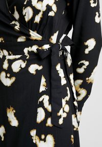 Vestido negro de corte envolvente con un lazo en la cintura, con un estampado abstracto de leopardo en crema y dorado y una textura de tela suave.