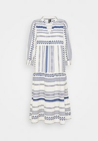 Lång, vit klänning med blå geometriska mönster. Har V-ringning och långa ärmar, samt detaljer med volanger på kjolen.