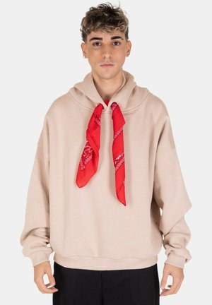 Hoodie oversize beige con tasca a marsupio e un bandana rossa annodata al collo, maniche lunghe e vestibilità rilassata.