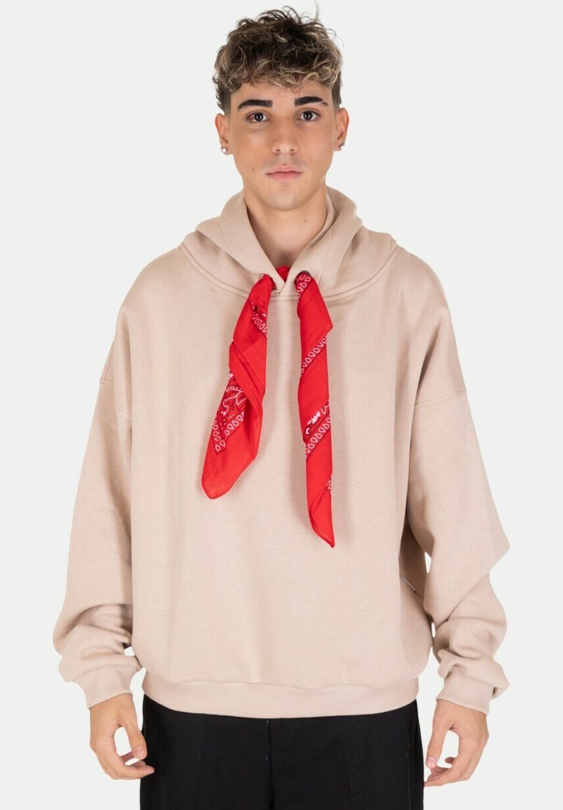 Hoodie oversize beige con tasca a marsupio e un bandana rossa annodata al collo, maniche lunghe e vestibilità rilassata.