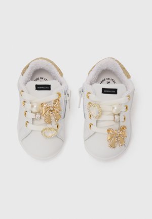 Chaussures en cuir blanc avec des accents dorés, ornées de nœuds décoratifs et de bijoux. Présentent un doublure texturée et un design à lacets.