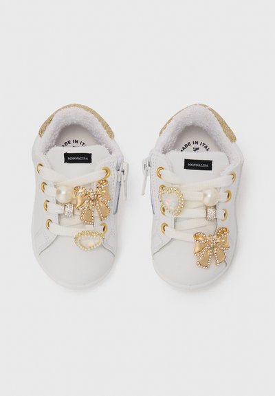 Chaussures en cuir blanc avec des accents dorés, ornées de nœuds décoratifs et de bijoux. Présentent un doublure texturée et un design à lacets.