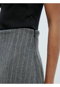 Jupe en laine grise avec un motif à rayures verticales, dotée d'une taille haute et d'un zip apparent sur le côté. Haut noir visible au-dessus.