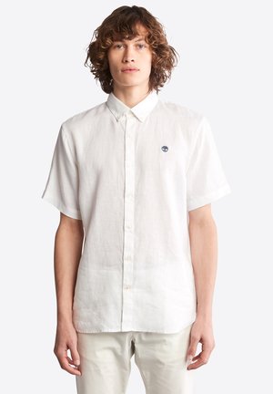Short-sleeve white linen shirt with a button-down collar and small embroidered logo on the chest. Smooth texture and relaxed fit.