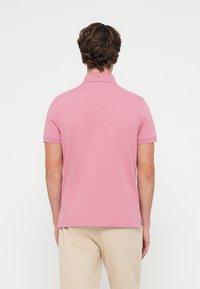 Polo marškiniai šviesiai rožinės spalvos, su apykakle, trumpomis rankovėmis ir tiesiu užlenkimu. Medžiaga glotni su nedideliu elastingumu.