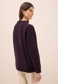 Paarse sweatshirt gemaakt van zacht materiaal, met een ronde hals, lange mouwen en geribde manchetten. Eenvoudig, ontspannen ontwerp zonder patronen of accenten.