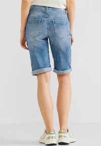 Light blue denim shorts with rolled cuffs, two back pockets, and contrast stitching. Worn with light-colored athletic shoes.