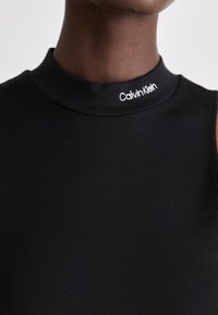 Black sleeveless top featuring a high collar, made of smooth fabric, with "Calvin Klein" embroidered in white at the neckline.
