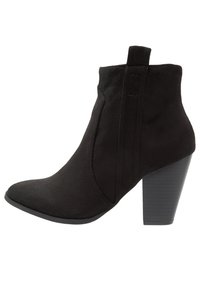 Czarny zamszowy botek za kostkę z szpiczastym noskiem i grubym, nawarstwionym obcasem, wyposażony w pętlę u góry ułatwiającą zakładanie.