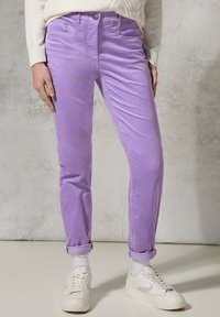 Lavendel katoenen chinos met een slim fit, omgerolde manchetten, zijzakken en een knoopsluiting, gecombineerd met witte sneakers en sokken.