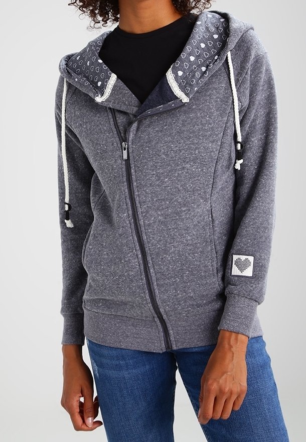 Felpa grigia con zip e cappuccio foderato, decorato con un motivo a cuori, corde regolabili e polsini a costine. Logo a forma di cuore sulla manica.