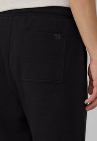 Pantalons de jogging noirs au design minimaliste, avec une poche arrière et une ceinture élastique. Le matériau semble doux avec une texture lisse.