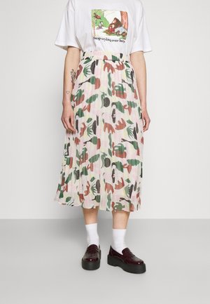 Personne portant un t-shirt blanc avec un motif d'ours, une jupe midi plissée aux motifs de feuilles vertes et marron, des chaussettes blanches et des chaussures à plateforme foncées.