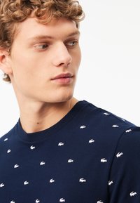 Marineblauw katoenen t-shirt met een ronde hals en verspreide witte geborduurde logo's. De stof heeft een gladde textuur en een aansluitend design.