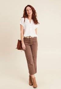 Witte kortefris shirts met knoopjes, bruine hoog-waist broek, beige enkellaarsjes en een bruine tas met franjes met een patroonstrip.