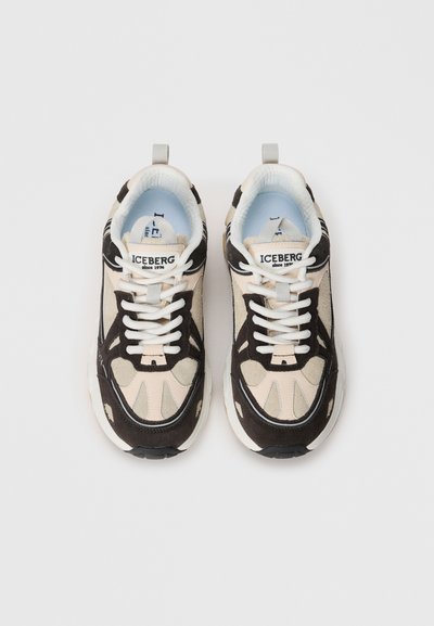 Beige och svarta sneakers med en texturerad mocka- och mesh-övre. Innehåller vita snören, en vadderad krage och distinkta sidomönster.