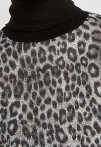 Czarny golf na szarej bluzce z wzorem w panterkę. Miękki, teksturowany materiał z ciemnymi plamami i prążkowanym dekoltem.