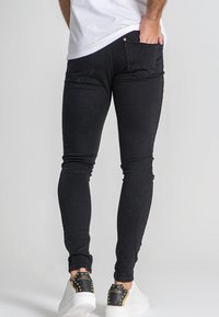 Jeans skinny negros con una textura suave, que cuentan con dos bolsillos traseros y detalles de costura sutiles, combinados con zapatillas blancas.