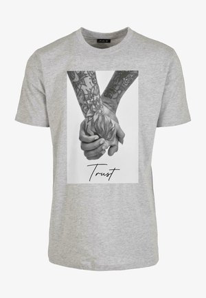 Grå bomullst-shirt med ett tryckt svartvitt foto av händer med intrikata tatueringar och ordet "Trust" i kursiv stil.