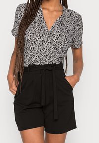 Pantalones cortos negros de talle alto con cintura ceñida, combinados con una blusa de mangas cortas de estampado floral blanco con escote en V.