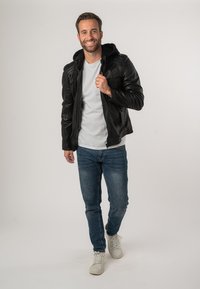 Zwart leren jack met een capuchon, gestructureerde schouders, gecombineerd met een witte T-shirt, blauwe spijkerbroek en witte sneakers.