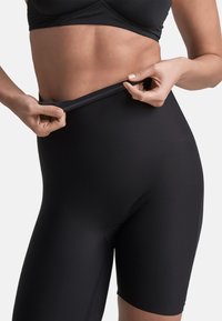 Shorts negros de cintura alta hechos de tejido elástico. Presentan una cinturilla suave y un diseño ajustado, terminando justo por encima de la rodilla.