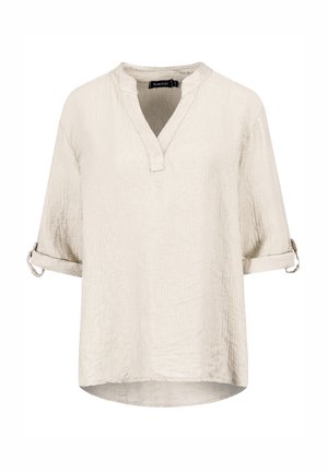 Light beige short-sleeve shirt made from textured fabric, featuring a V-neckline and rolled cuffs. Subtle pattern across the surface.