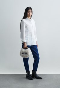 Witte blouse met lange mouwen en knoopdetails, blauwe jeans, zwarte enkellaarzen en een grijze bont handtas met het "Moschino" logo.