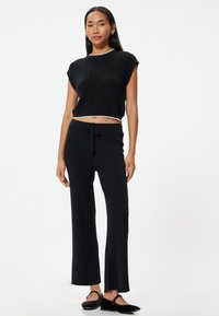 Zwarte geribbelde crop top met een witte rand, gecombineerd met zwarte wijde broek met een trekkoord in de taille en een gladde textuur.