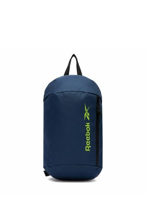 Bolso bandolera azul marino de Reebok con bolsillo vertical con cremallera y logo verde lima, asa negra en la parte superior, de pie sobre fondo blanco.