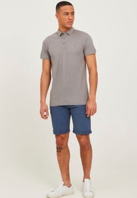 Gray short-sleeve polo shirt with three-button placket, worn with blue denim shorts. Model wearing white sneakers, showing a tattoo on the leg.