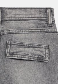 Gray denim jeans back pocket with stitched detailing, metal rivet, and label reading "NAME IT DENIM." Textured fabric with a faded finish.