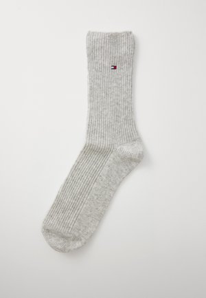 Ein einzelner hellgrauer gerippter Socken mit kleinem rot-weißen und blauen rechteckigen Logo am oberen Knöchelbereich.