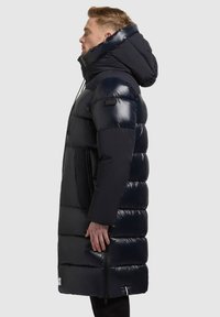Abrigo de plumas navy con capucha, que presenta una textura brillante, bolsillos laterales con cremallera y un diseño hasta la rodilla, proporcionando aislamiento y cobertura.