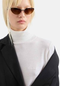 Maglione bianco a collo alto abbinato a un blazer nero. La modella indossa occhiali da sole a forma di gatto scuri, che accentuano il contrasto di questo outfit strutturato.