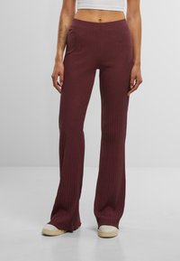 Pantalons évasés en tricot côtelé bordeaux avec une taille haute et une finition texturée, associés à des baskets de sport blanches.