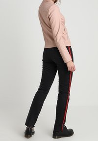 Giacca in pelle sintetica rosa chiaro con dettagli trapuntati, abbinata a jeans neri con strisce laterali rosse e stivali neri con lacci.