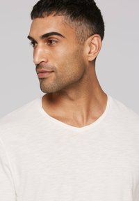 Weißes, kurzärmeliges T-Shirt mit V-Ausschnitt und strukturiertem Stoff. Es weist ein dezentes Melanmuster auf und besticht durch ein weiches, lässiges Design.