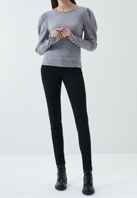 Maglione grigio con maniche a sbuffo e bottoni decorativi ai polsini, abbinato a pantaloni skinny neri e stivali neri con lacci.