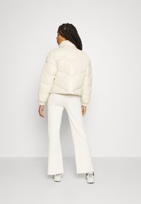 Cream puffer jacket with a high collar, featuring a quilted design and elastic cuffs, paired with white flared pants and patterned sneakers.
