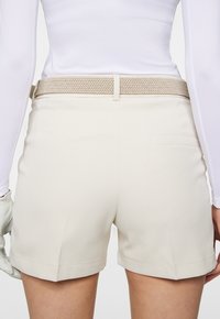 Beżowe szorty z plecionym jasnobeżowym paskiem, z jedną tylną kieszenią, dopasowany krój i gładka faktura materiału.