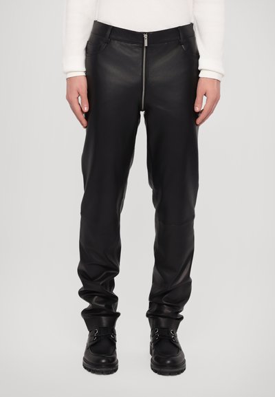 Zwarte leren broek met een slim fit en een rits aan de voorkant. Kenmerkt zich door een gladde textuur en een minimalistisch ontwerp, aangevuld met donkere, platte laarzen.