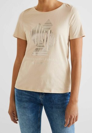 Beżowa bawełniana koszulka z krótkim rękawem, ozdobiona geometrycznym srebrnym wzorem i napisem "WONDER.LOVE.REPEAT." nad krawędzią.
